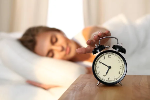 Mujer joven soñolienta extendiendo la mano a la alarma sonando dispuesto a apagarlo. Despertarse temprano, no dormir lo suficiente, conseguir el concepto de trabajo. —  Fotos de Stock