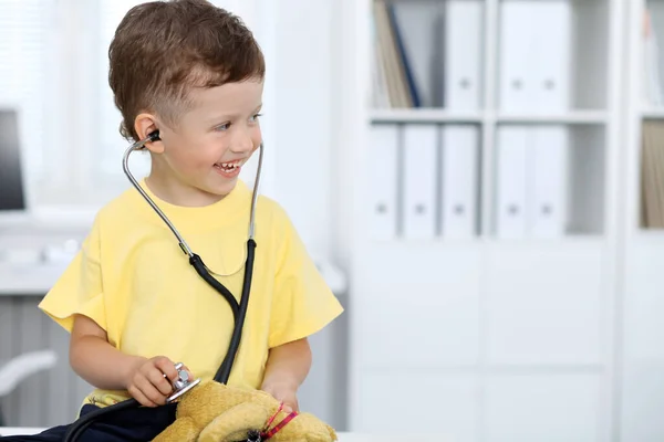 Dottore e paziente in ospedale. Buon bambino che si diverte mentre viene esaminato con lo stetoscopio. Concetto sanitario e assicurativo — Foto Stock