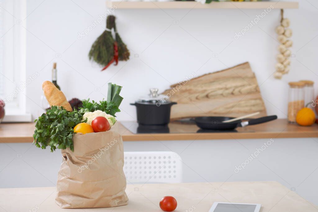 Paper bag full of vegetables on the table in kitchen interiors. Healthy meal and vegetarian concept.
