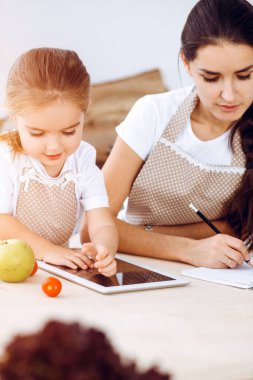 Mutlu kadın ve kızı aile ziyafeti, güneşli mutfak için yeni tarifler arıyorlar. Noel, yeni yıl, Şükran Günü, yıldönümü, anneler günü. Sağlıklı yemek pişirme kavramı.