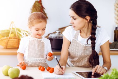 Mutlu kadın ve kızı aile ziyafeti, güneşli mutfak için yeni tarifler arıyorlar. Noel, yeni yıl, Şükran Günü, yıldönümü, anneler günü. Sağlıklı yemek pişirme kavramı.