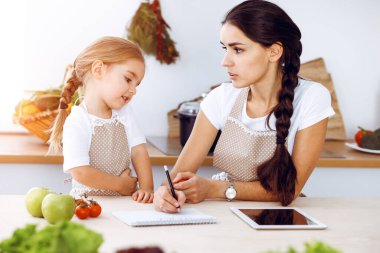 Mutlu kadın ve kızı aile ziyafeti, güneşli mutfak için yeni tarifler arıyorlar. Noel, yeni yıl, Şükran Günü, yıldönümü, anneler günü. Sağlıklı yemek pişirme kavramı.