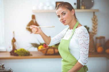 Çekici, genç, koyu renk saçlı bir kadın. Güneşli mutfakta ayakta durup gülümserken yeni keto tarifi ile solucan tavasında yemek pişiriyor. Yemek pişirme ve ev idaresi kavramları.