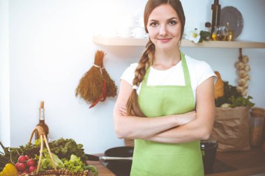 Çekici genç bir kadın, güneşli mutfakta dururken lezzetli bir salata karışımı için yeni bir tarif hazırlamaya hazır..