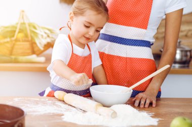 Mutlu kadın ve kızı, güneşli mutfakta ziyafet veren lezzetli bir aile için hamur yoğurup kurabiye pişiriyorlar. Noel, yeni yıl, Şükran Günü, yıldönümü, anneler günü. Sağlıklı yemek pişirme kavramı.