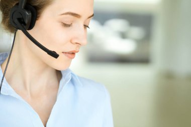 Kulaklıklı güzel bir kadın uzman müşterilere online olarak yardım ediyor ve modern çağrı merkezinde büyüleyici bir şekilde gülümsüyor. İş adamları konsepti.