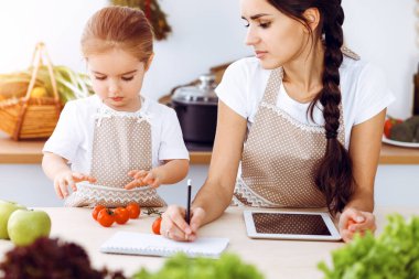 Mutlu kadın ve kızı aile ziyafeti, güneşli mutfak için yeni tarifler arıyorlar. Noel, yeni yıl, Şükran Günü, yıldönümü, anneler günü. Sağlıklı yemek pişirme kavramı.