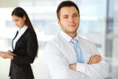 Kendine güvenen orta yaşlı bir iş adamının portresi modern bir ofiste meslektaşıyla arka planda duruyor. İş konsepti.