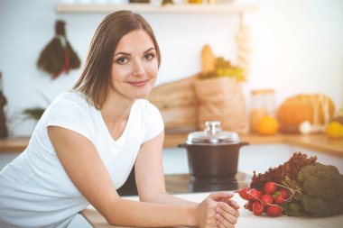 Çekici genç bir kadın, güneşli mutfakta masada otururken lezzetli bir salata karışımı için yeni bir tarif hazırlamaya hazır..