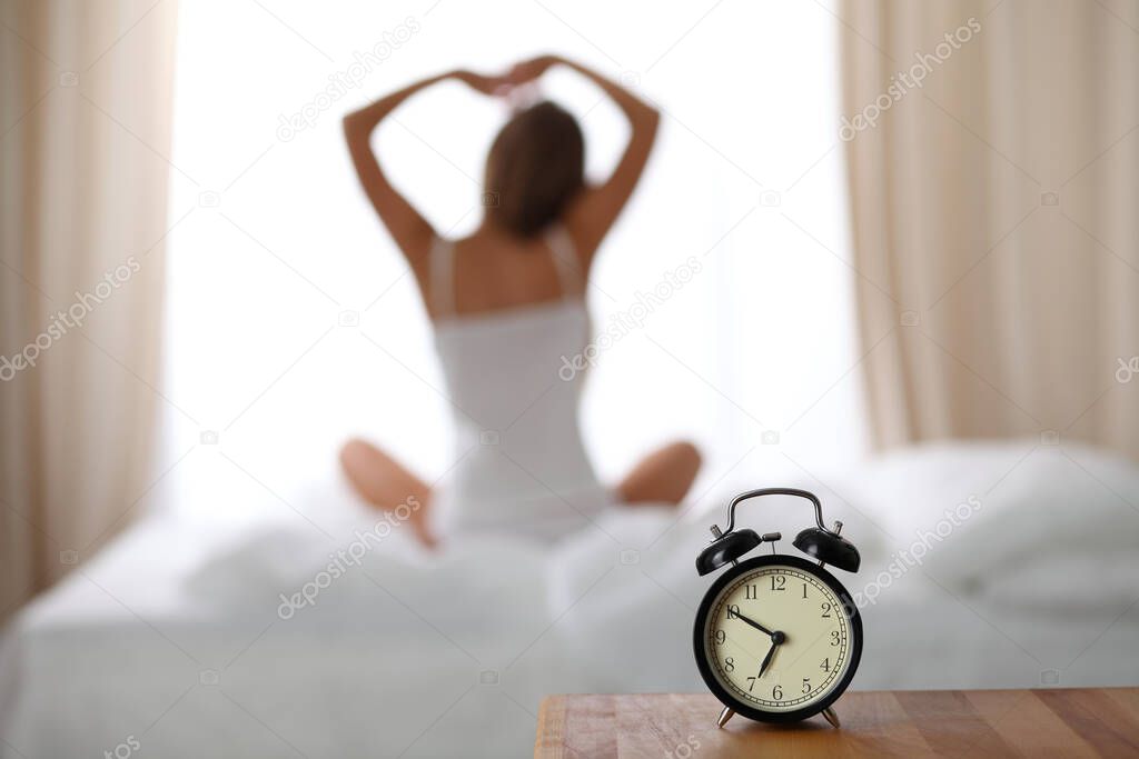 Woman stretching in bed after wake up, back view, entering a day happy and relaxed after good night sleep. Sweet dreams, good morning, new day, weekend, holidays concept.