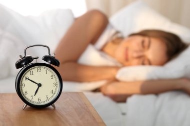 Yatakta rahat ve mutlu bir şekilde yatarken uyuyan ve gülümseyen güzel genç bir kadın çalar saatin arka planında çalacak. Gün ışığı yüzünü aydınlatıyor..