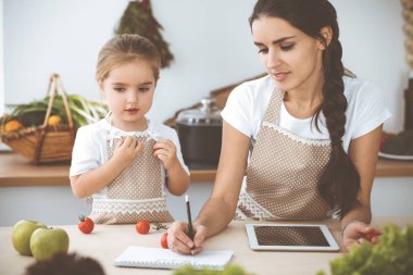 Mutlu kadın ve kızı lezzetli bir aile ziyafeti için yeni tarifler arıyorlar. Noel, yeni yıl, Şükran Günü, yıldönümü, anneler günü. Sağlıklı yemek pişirme kavramı.