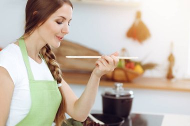 Çekici genç bir kadın, güneşli mutfakta ayakta durup gülümserken yeni keto tarifiyle çorba hazırlıyor. Yemek pişirme ve ev idaresi kavramları.