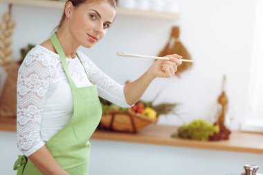 Çekici, genç, koyu renk saçlı bir kadın. Güneşli mutfakta ayakta durup gülümserken yeni keto tarifi ile solucan tavasında yemek pişiriyor. Yemek pişirme ve ev idaresi kavramları.