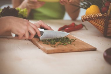 Mutfak masasında otururken ve gülümserken lezzetli bir vejetaryen salatası için sebze dilimleyen bilinmeyen genç kadın, sadece eller, yakın çekim. Yemek pişirme konsepti.