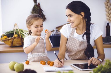Mutlu kadın ve kızı lezzetli bir aile ziyafeti için yeni tarifler arıyorlar. Noel, yeni yıl, Şükran Günü, yıldönümü, anneler günü. Sağlıklı yemek pişirme kavramı.