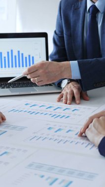 Masada oturan işadamı, mali verileri tartışırken mali tablolara, iş arkadaşlarıyla ofis toplantılarında pazar eğilimlerini işaret ediyor. İş adamları konsepti.