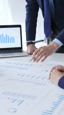 Masanın yanında duran ve mali verileri tartışırken mali tablolara işaret eden bir işadamı, ofiste yapılan bir şirket toplantısında iş arkadaşlarıyla pazar eğilimleri. İş adamları konsepti.