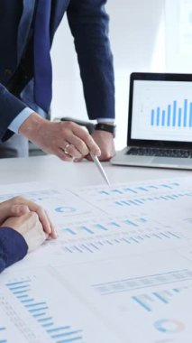 Masanın yanında duran ve mali verileri tartışırken mali tablolara işaret eden bir işadamı, ofiste yapılan bir şirket toplantısında iş arkadaşlarıyla pazar eğilimleri. İş adamları konsepti.