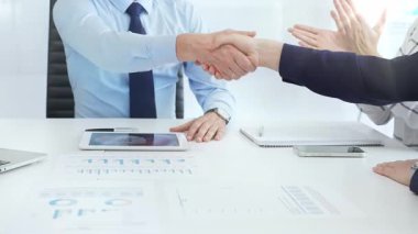 İş anlaşmasını sonuçlandıran profesyonel meslektaşlar, ellerini konferans masasına dijital cihazlar ve sözleşmeyle kenetleyerek başarılı bir kurumsal pazarlığın sinyallerini veriyorlar. El sıkışın.