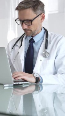 Beyaz önlük ve steteskop giyen doktor dizüstü bilgisayarda çalışıyor, teletıp danışmanlığı yapıyor ya da tıbbi rapor yazıyor. İlaç ve sağlık hizmetleri