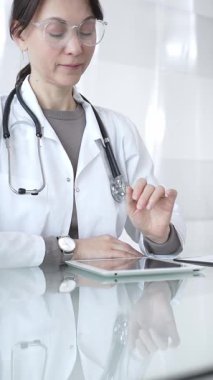 Steteskoplu beyaz önlüklü bir tıp uzmanı dijital sağlık hizmetleri, teletıp ve EMR veri incelemesi ve danışma için bir tablet kullanıyor. İlaç ve sağlık hizmetleri