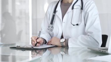 Panoya yazı yazan, steteskop takan, ilaç, sağlık, teşhis ve tedavi kavramlarını yansıtan beyaz önlüklü bir doktor. İlaç ve sağlık hizmetleri