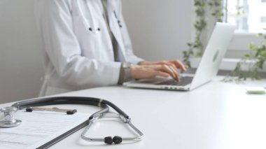 Stetoskop ve tıbbi kayıtlar doktorun karşısındaki masada. Bilgisayarında tıbbi bir büro var. İnternet üzerinden sağlık hizmeti ya da teletıp hizmeti sunuyor. Tıp konsepti.