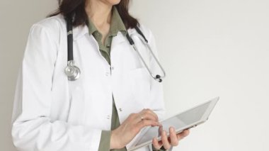 Yeşil bluz ve steteskop üzerine beyaz önlük giyen kimliği belirsiz profesyonel doktor dijital tablet kullanıyor. Bu da tıpta yenilikçi sağlık uygulamaları olduğunu gösteriyor. Sağlık hizmeti kavramı.