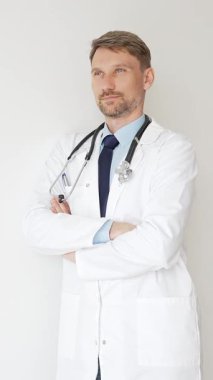 Kendine güvenen erkek doktor kolları çapraz duruyor, steteskop ve beyaz önlük giyiyor. Düşünceli bir şekilde, tıp alanında profesyonelliği ve uzmanlığı somutlaştırıyor. İlaç ve sağlık hizmetleri