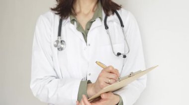 Stetoskop ve yeşil bluzun üzerine beyaz önlük giyen kimliği belirsiz bir kadın doktor tahta renkli bir panoya tıbbi uzmanlığı ve hasta bakımını temsil eden bir yazı yazıyor. Tıp konsepti