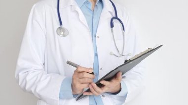 Mavi bluzun üzerine steteskop ve beyaz önlük giyen kimliği belirsiz kadın doktor tıbbi uzmanlığı ve hasta bakımını temsil eden siyah bir panoya yazı yazıyor. Tıp konsepti.