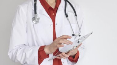 Tuğla kırmızısı bluz ve stetoskop üzerine beyaz önlük giyen kimliği belirsiz profesyonel doktor dijital tablet kullanıyor. Bu da tıpta yenilikçi sağlık uygulamaları olduğunu gösteriyor. Sağlık hizmeti kavramı