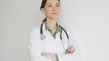Laboratuvar önlüğü ve steteskop giyen kadın tıp uzmanı kollarını kavuşturarak güvenle duruyor. Sağlık sektöründe profesyonellik ve uzmanlık yayıyor. İlaç ve sağlık hizmetleri
