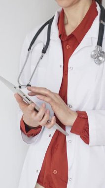Tuğla kırmızısı bluz ve stetoskop üzerine beyaz önlük giyen kimliği belirsiz profesyonel doktor dijital tablet kullanıyor. Bu da tıpta yenilikçi sağlık uygulamaları olduğunu gösteriyor. Sağlık hizmeti kavramı