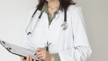 Yeşil bluz üzerine steteskop ve beyaz önlük giyen kimliği belirsiz kadın doktor tıbbi uzmanlığı ve hasta bakımını temsil eden bir panoya yazı yazıyor. İlaç ve sağlık hizmetleri kavramı.