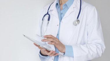 Mavi bluz ve steteskop üzerine beyaz önlük giyen kimliği belirsiz kadın doktor dijital tablet kullanıyor. Bu da tıpta yenilikçi sağlık uygulamaları olduğunu gösteriyor. Sağlık ve Tıp Konsepti.