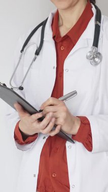 Tuğla kırmızı bluzun üzerine steteskop ve beyaz önlük giyen kimliği belirsiz kadın doktor tıbbi uzmanlığı ve hasta bakımını temsil eden bir panoya yazı yazıyor. İlaç ve sağlık hizmetleri kavramı.