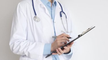 Mavi bluzun üzerine steteskop ve beyaz önlük giyen kimliği belirsiz kadın doktor tıbbi uzmanlığı ve hasta bakımını temsil eden siyah bir panoya yazı yazıyor. Tıp konsepti.