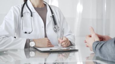 Klinikteki hasta muayenesi sırasında panoya not alan beyaz önlüklü doktor sağlık, teşhis ve bakım kararlarına odaklanmış. İlaç ve sağlık hizmetleri