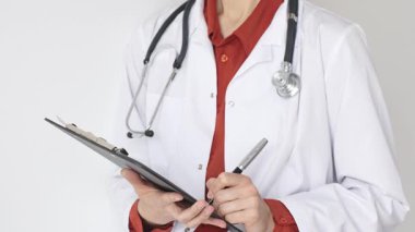 Tuğla kırmızı bluzun üzerine steteskop ve beyaz önlük giyen kimliği belirsiz kadın doktor tıbbi uzmanlığı ve hasta bakımını temsil eden bir panoya yazı yazıyor. İlaç ve sağlık hizmetleri kavramı.