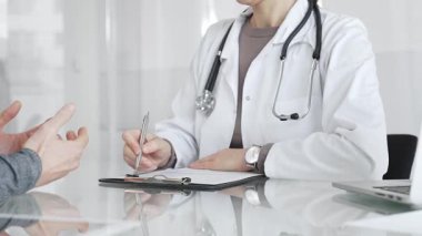 Klinikteki hasta muayenesi sırasında panoya not alan beyaz önlüklü doktor sağlık, teşhis ve bakım kararlarına odaklanmış. İlaç ve sağlık hizmetleri