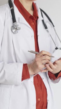 Tuğla kırmızı bluzun üzerine steteskop ve beyaz önlük giyen kimliği belirsiz kadın doktor tıbbi uzmanlığı ve hasta bakımını temsil eden bir panoya yazı yazıyor. İlaç ve sağlık hizmetleri kavramı.