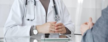 Klinik muayenesi sırasında bir hastaya tıbbi bilgileri açıklarken el hareketi yapan beyaz önlüklü kadın bir doktor. İlaç ve sağlık hizmetleri