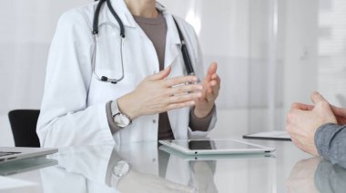 Klinik muayenesi sırasında bir hastaya tıbbi bilgileri açıklarken el hareketi yapan beyaz önlüklü kadın bir doktor. İlaç ve sağlık hizmetleri