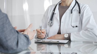 Klinikteki hasta muayenesi sırasında panoya not alan beyaz önlüklü doktor sağlık, teşhis ve bakım kararlarına odaklanmış. İlaç ve sağlık hizmetleri