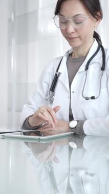 Steteskoplu beyaz önlüklü bir tıp uzmanı dijital sağlık hizmetleri, teletıp ve EMR veri incelemesi ve danışma için bir tablet kullanıyor. İlaç ve sağlık hizmetleri