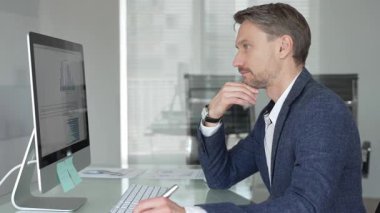 Düşünceli iş adamı stratejik planlamaya odaklanmış, modern ofis ortamında bilgisayar ve evrak işleriyle masa başında notlar yazıyor. İş adamları konsepti