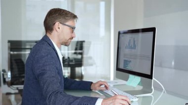 Profesyonel iş adamı gözlük takıyor ve spor ceket giyiyor, çağdaş bir ofis ortamında çalışıyor, bir masaüstü bilgisayarında görevler yapıyor. İş adamları konsepti