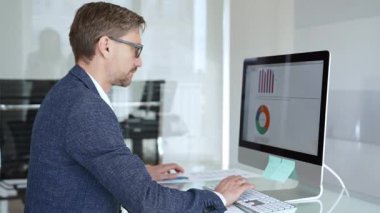 Profesyonel iş adamı gözlük takıyor ve spor ceket giyiyor, çağdaş bir ofis ortamında çalışıyor, bir masaüstü bilgisayarında görevler yapıyor. İş adamları konsepti